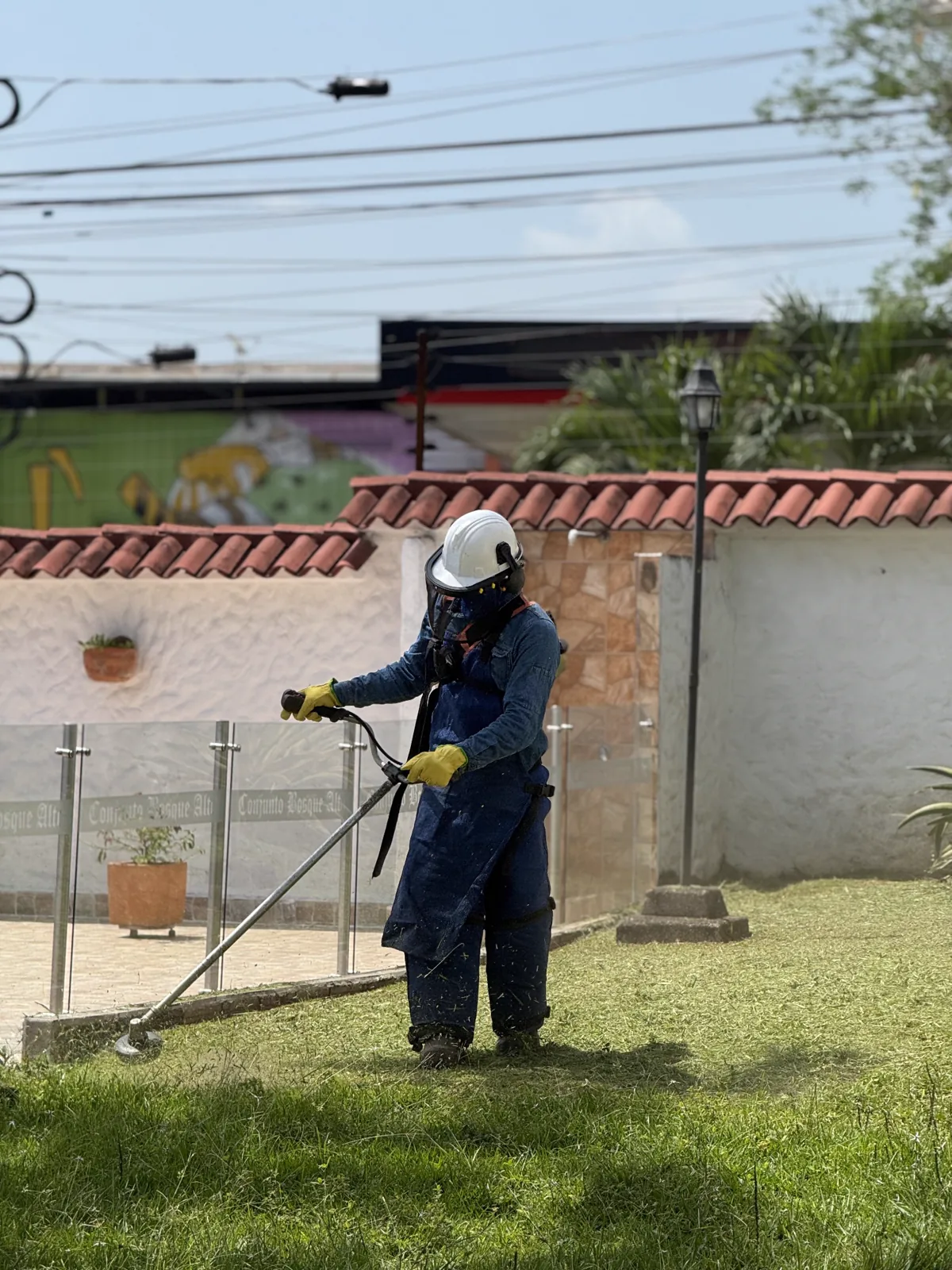 Persona con casco, visor y guantes utiliza una guadaña sobre el césped